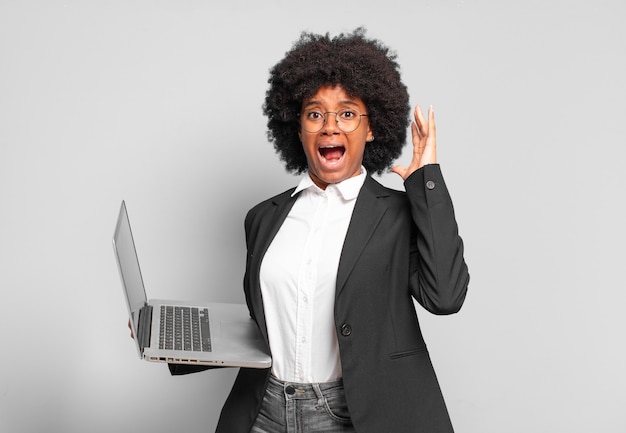 Giovane donna d'affari afro che urla con le mani in alto, sentendosi furiosa, frustrata, stressata e turbata. concetto di business