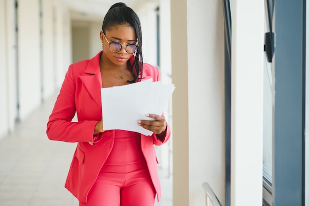 Giovane donna d'affari afroamericana elegante attraente in abbigliamento formale al corridoio dell'ufficio.