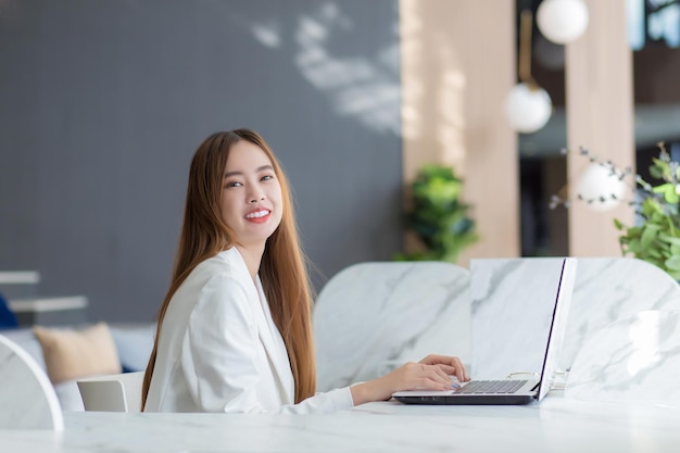 Giovane donna d'affari asiatica che lavora in uno spazio di coworking con lavoro di ufficio su laptop Concetto di donna d'affari