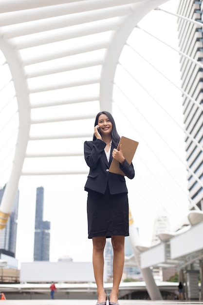 Giovane donna d'affari asiatica professionale intelligente che utilizza il telefono cellulare in città all'aperto