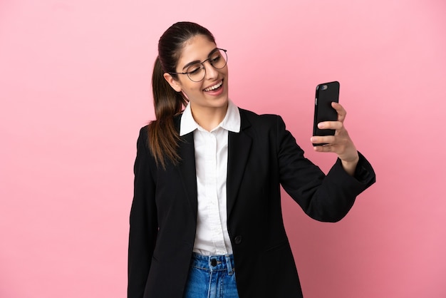 Giovane donna d'affari caucasica isolata su sfondo rosa facendo un selfie