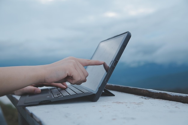 Giovane donna d'affari che lavora al computer in un bar sulla roccia Giovane ragazza che lavora al computer portatile al tramonto o all'alba sulla cima della montagna al mare giornata di lavoro