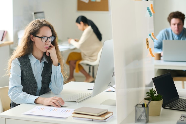 Giovane donna d'affari che lavora al suo posto di lavoro al computer in ufficio con i suoi colleghi sullo sfondo