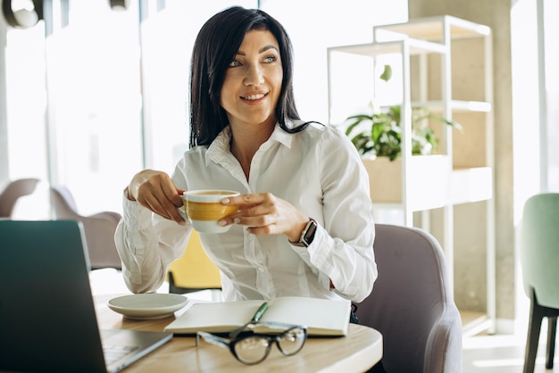 Giovane donna d'affari che lavora in ufficio al computer e che beve caffè