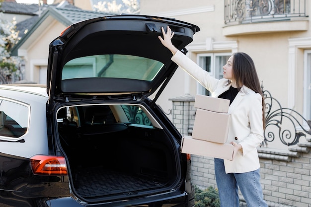 Giovane donna d'affari che ritira i pacchi da un bagagliaio di un'auto che torna a casa in auto La ragazza preme un pulsante per chiudere il bagagliaio Concetto di acquisto di merci online e consegna a casa