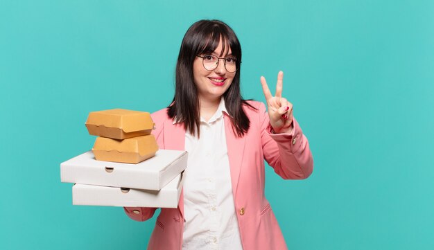 Giovane donna d'affari che sorride e sembra felice, spensierata e positiva, gesticolando vittoria o pace con una mano