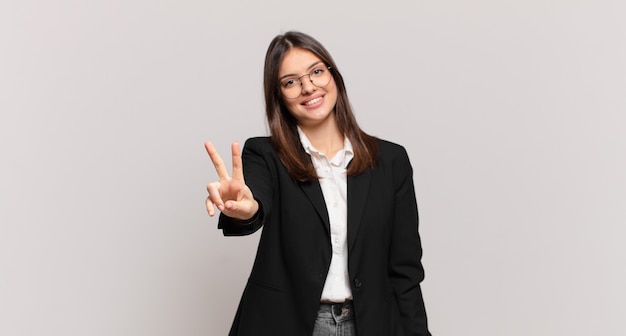 giovane donna d'affari che sorride e sembra felice, spensierata e positiva, gesticolando vittoria o pace con una mano