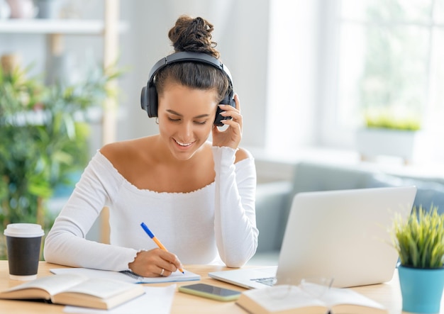 Giovane donna d'affari che studia online, guarda webinar, podcast sul laptop, prende appunti, seduto alla scrivania. Concetto di e-learning.