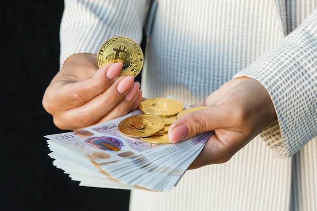 Giovane donna d'affari che tiene in mano sterline britanniche e bitcoin in primo piano di mani femminili con equivalenti di denaro contante