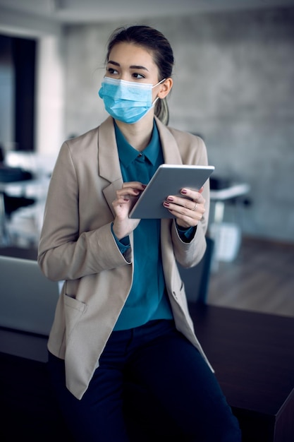 Giovane donna d'affari che utilizza il touchpad mentre indossa la maschera facciale in ufficio