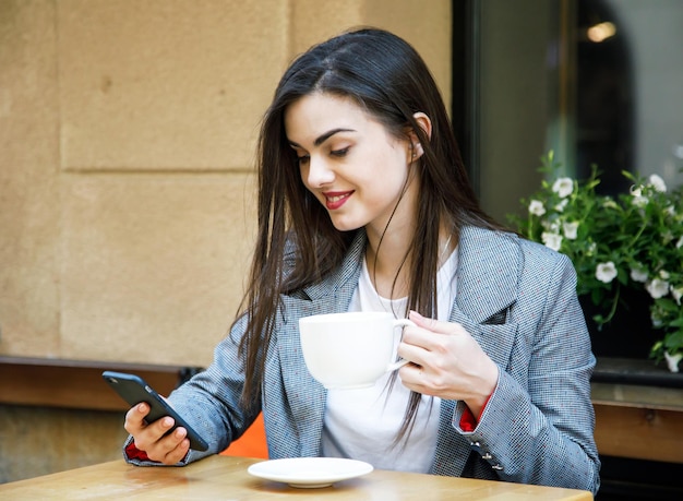 Giovane donna d'affari che utilizza smartphone mentre beve caffè alla caffetteria di strada