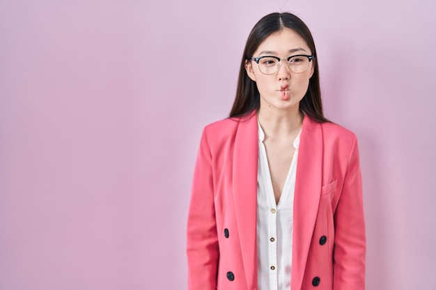 Giovane donna d'affari cinese con gli occhiali che fa la faccia di pesce con le labbra, gesto folle e comico. espressione buffa.
