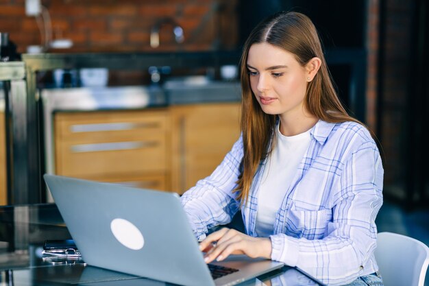 Giovane donna d'affari concentrata in occhiali e maglietta che lavora con il computer portatile a casa