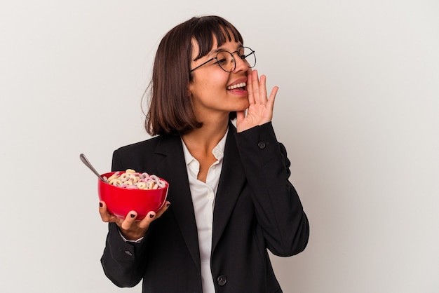 Giovane donna d'affari di razza mista che mangia cereali isolati su sfondo bianco gridando e tenendo il palmo vicino alla bocca aperta.