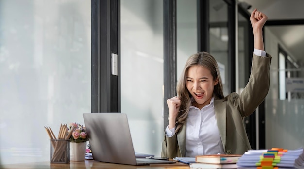 Giovane donna d'affari di successo alzando le mani e ridendo di felicità seduto alla sua scrivania officex9