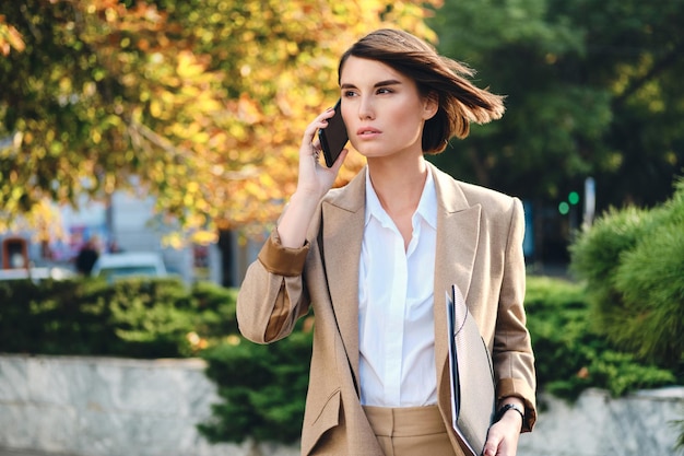 Giovane donna d'affari elegante e attraente che parla sul cellulare distogliendo lo sguardo sulla strada della città