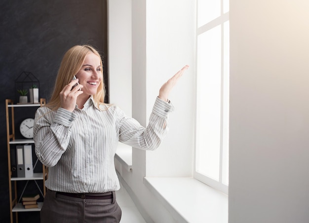 Giovane donna d'affari emotiva che parla al telefono dalla finestra in ufficio