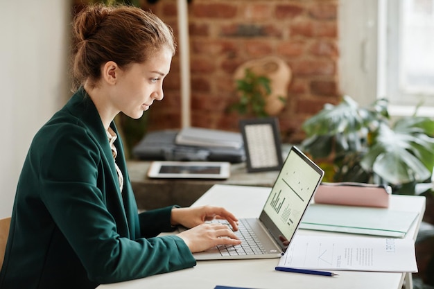 Giovane donna d'affari fiduciosa in abiti formali che digitano sulla tastiera del computer portatile