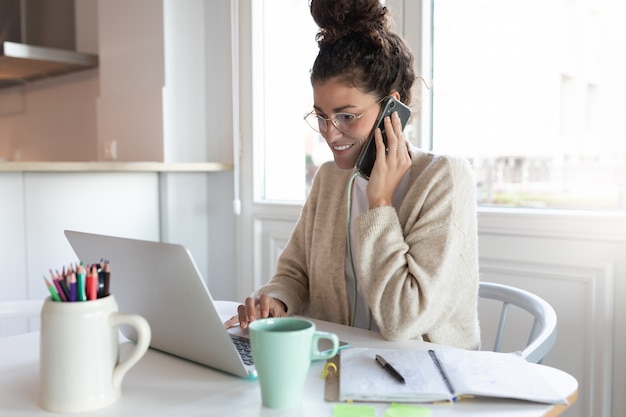 Giovane donna d'affari in bicchieri lavorando sul computer portatile da casa. Lavoro remoto. tazza di caffè / tè sul tavolo. Comunicare con i clienti online.