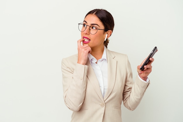 Giovane donna d'affari in possesso di un telefono cellulare isolato su sfondo bianco rilassato pensando a qualcosa guardando uno spazio di copia.