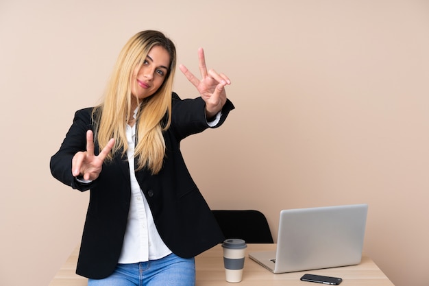 Giovane donna d'affari in un ufficio sorridente e mostrando il segno della vittoria