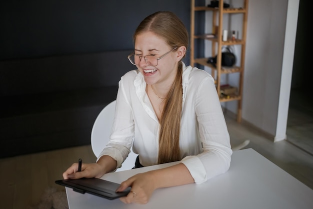 Giovane donna d'affari in una camicia bianca e occhiali ride tenendo un tablet nelle sue mani