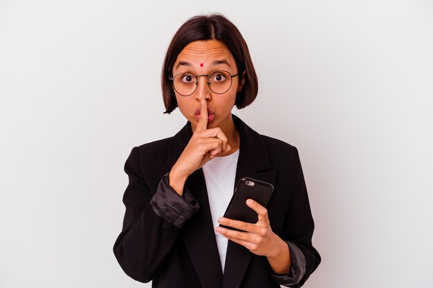 Giovane donna d'affari indiana che tiene un telefono isolato mantenendo un segreto o chiedendo silenzio.