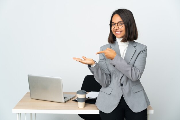 Giovane donna d'affari latino che lavora in un ufficio isolato su sfondo bianco tenendo copyspace immaginario sul palmo per inserire un annuncio