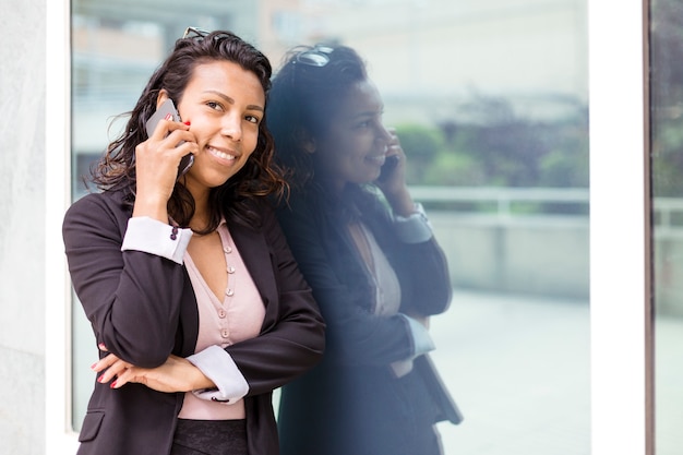 Giovane donna d'affari latinoamericana che parla al telefono nel suo posto di lavoro. Spazio per il testo.