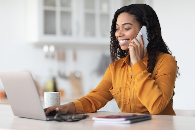 Giovane donna d'affari nera che lavora da casa avendo una conversazione telefonica