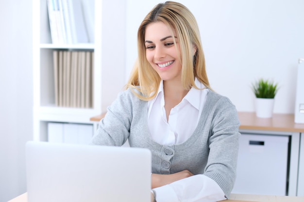 Giovane donna d'affari o studentessa seduta sul posto di lavoro in ufficio con un computer portatile. Concetto di affari domestici.
