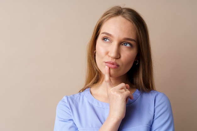 Giovane donna d'affari pensierosa che pensa a qualche idea su sfondo beige