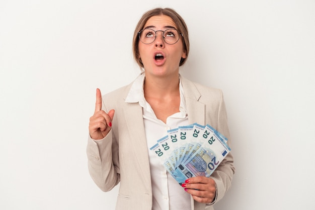 Giovane donna d'affari russa che tiene banconote isolate su sfondo bianco rivolto verso l'alto con la bocca aperta.
