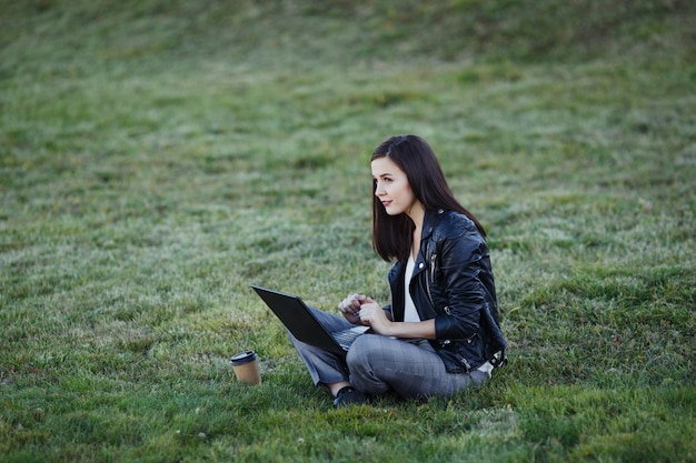 Giovane donna d'affari seduto e lavorando nel parco con il portatile