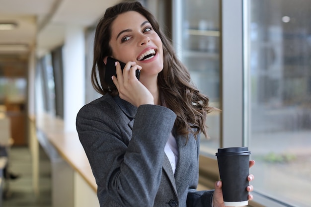 Giovane donna d'affari sorridente che utilizza smartphone vicino al computer in ufficio.