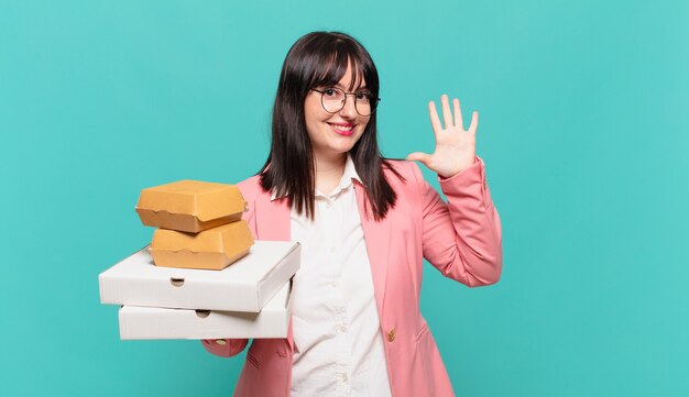 Giovane donna d'affari sorridente e dall'aspetto amichevole, mostrando il numero cinque o il quinto con la mano in avanti, conto alla rovescia