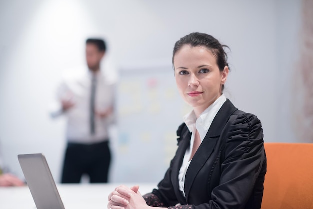 giovane donna d'affari sulla riunione del computer portatile usineg, gruppo blured di persone in background all'interno dell'ufficio di avvio moderno e luminoso che prende appunti sulla lavagna bianca e fa brainstorming sui piani un