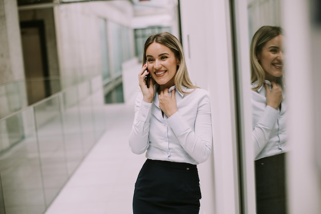 Giovane donna d'affari utilizzando il telefono cellulare nel corridoio dell'ufficio