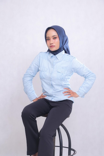 Giovane donna d'ufficio indonesiana che indossa una camicia blu hijab seduta in una sedia elegante con le mani che lo tengono