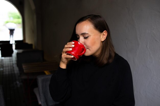 giovane donna da sola che beve un drink in un caffè con terrazza in una giornata piovosa