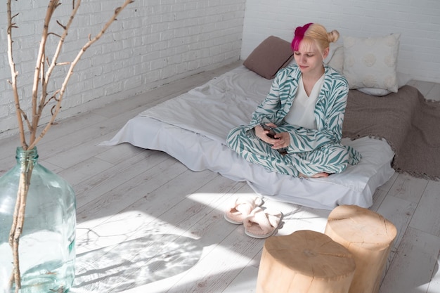 giovane donna dai capelli rosa seduta sul letto guardando lo schermo dello smartphone a casa