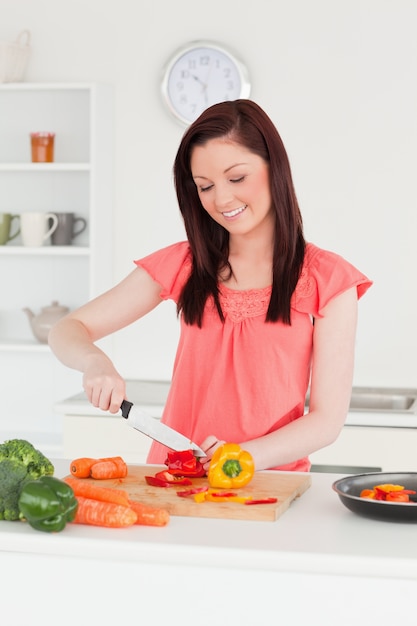 Giovane donna dai capelli rossi attraente tagliare alcune carote in cucina