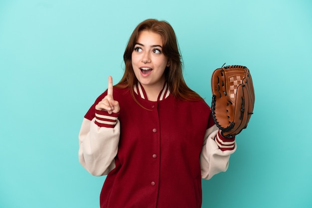 Giovane donna dai capelli rossi che gioca a baseball isolata su sfondo blu pensando a un'idea che punta il dito verso l'alto