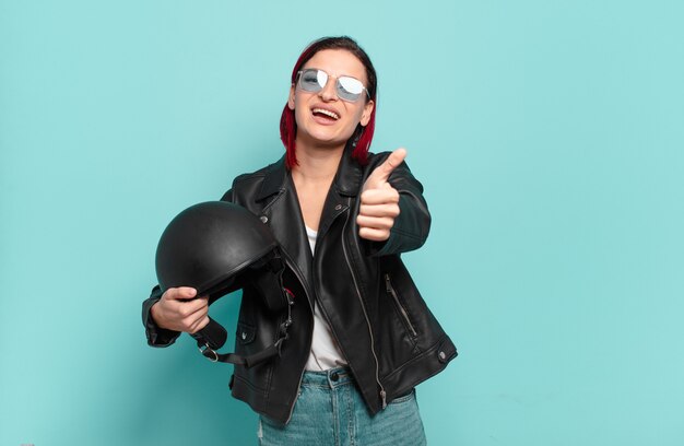 Giovane donna dai capelli rossi che si sente orgogliosa, spensierata, sicura e felice, sorridendo positivamente con i pollici in su.