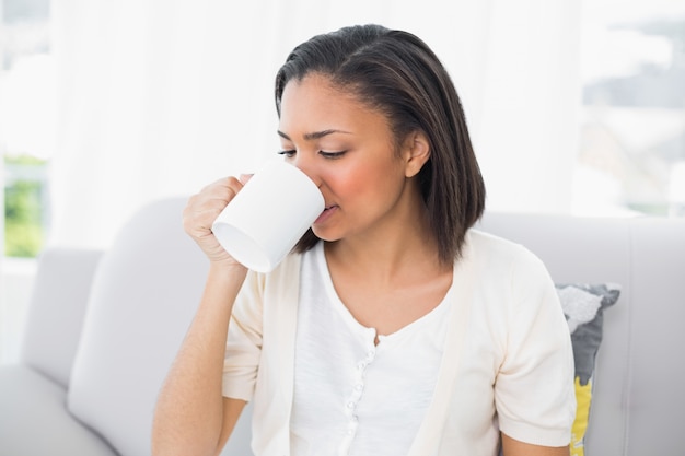 Giovane donna dai capelli scuri attraente in vestiti bianchi che beve caffè