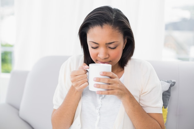 Giovane donna dai capelli scuri pacifica in vestiti bianchi che gode del caffè