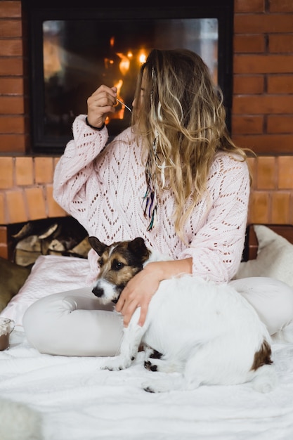 Giovane donna davanti al camino beve cacao con marshmello con cane.