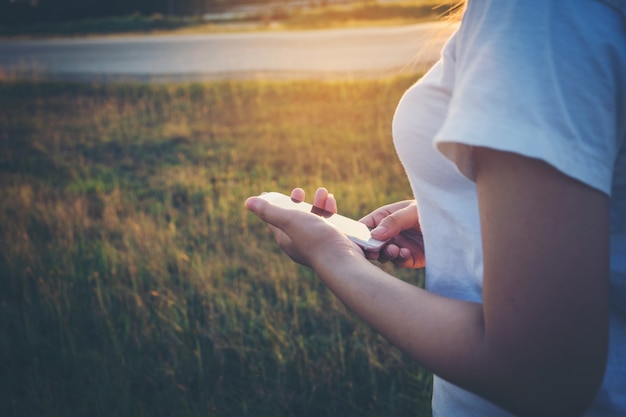 Giovane donna dei pantaloni a vita bassa che utilizza uno Smart Phone del touch screen nel tramonto.