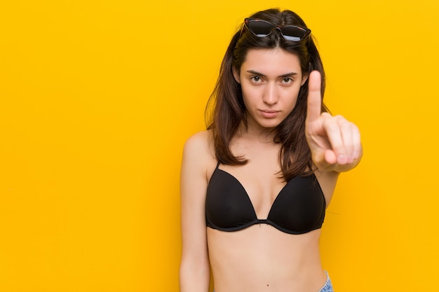 Giovane donna del brunette che porta un bikini contro la priorità bassa gialla