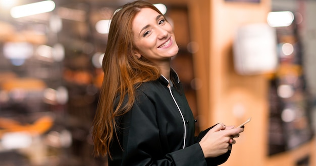 Giovane donna del cuoco unico di redhead che invia un messaggio con il cellulare nel forno
